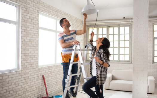 Couple installing a new light fixture during a home renovation project, enhancing their property’s appeal for rental in Phuket.