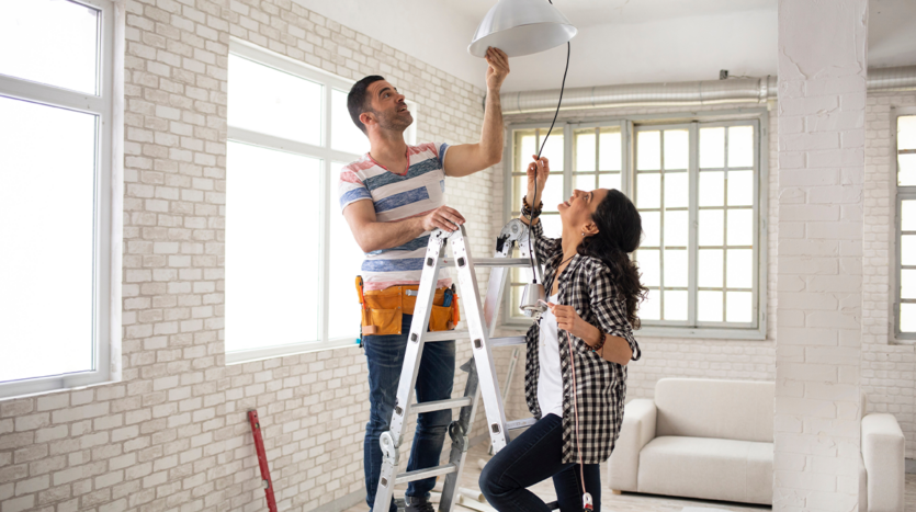 Couple installing a new light fixture during a home renovation project, enhancing their property’s appeal for rental in Phuket.